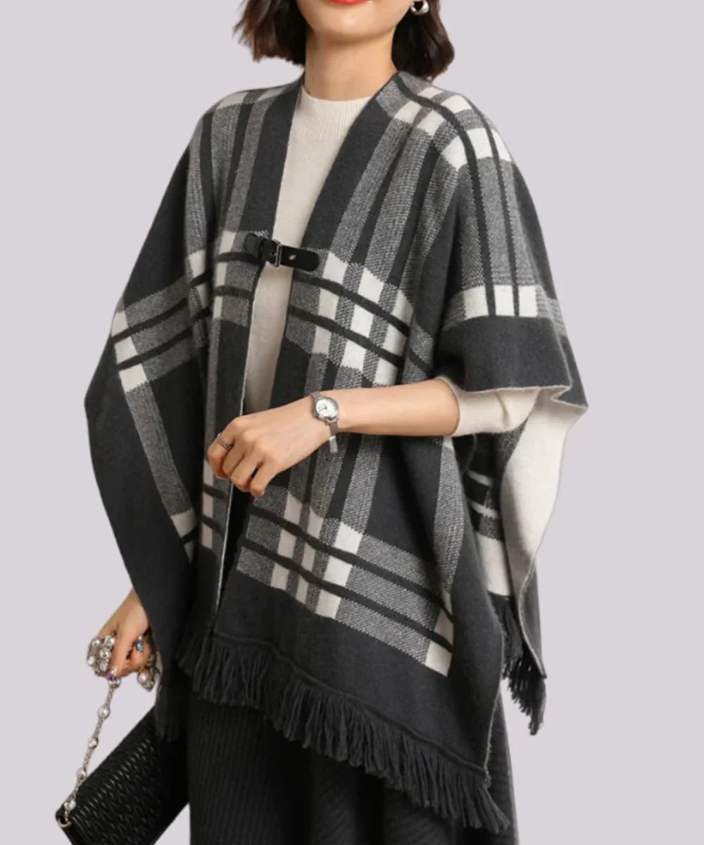 Poncho en cachemire noir à carreaux, franges et attache boucle, porté par une femme élégante