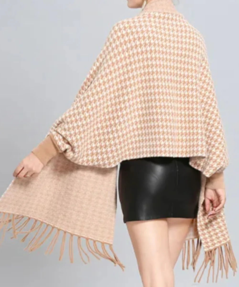 Poncho cape beige à motifs pied-de-poule et franges, porté sur jupe courte noire.