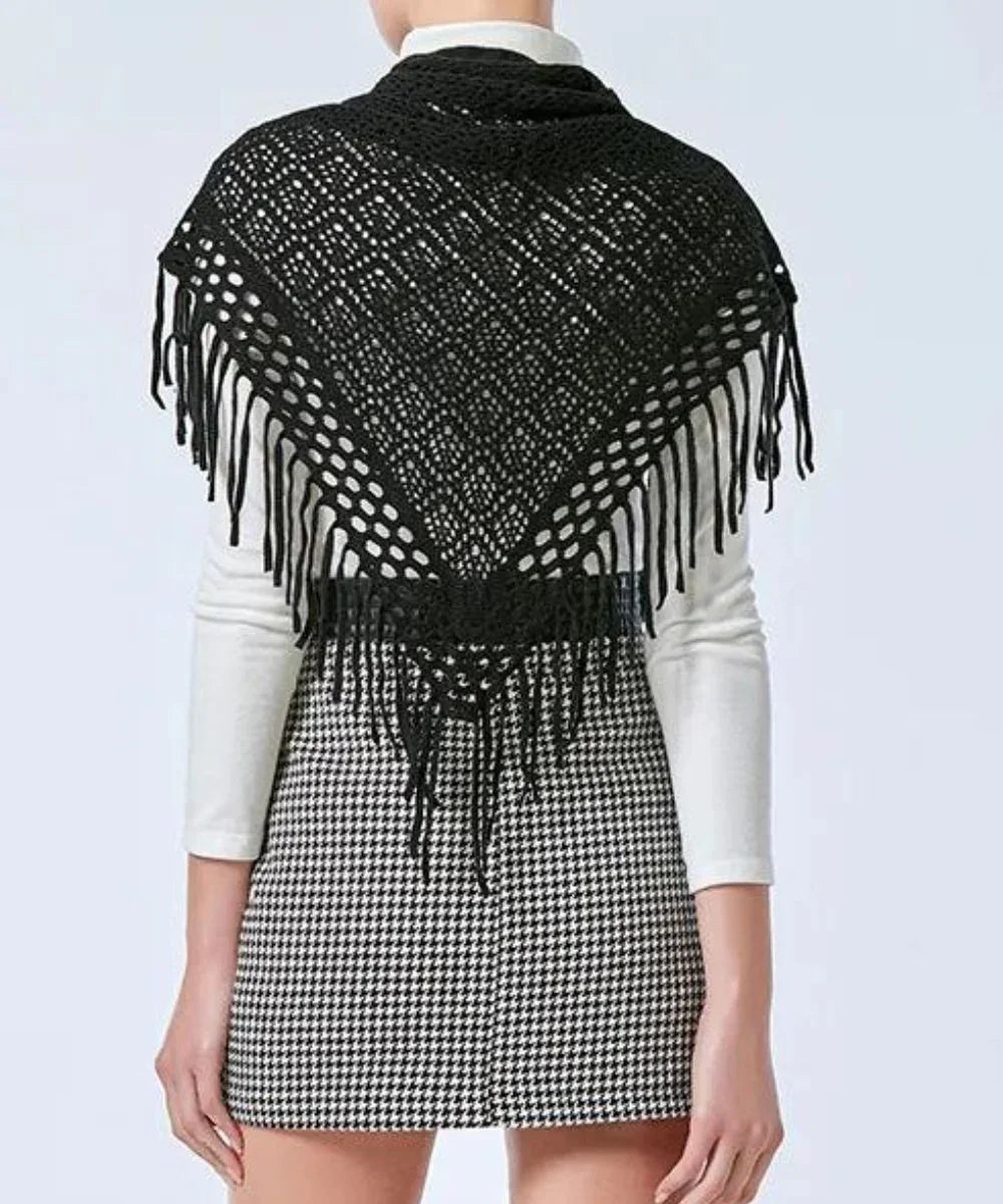 Poncho court noir en maille ajourée à franges, porté sur un haut blanc et une jupe à carreaux