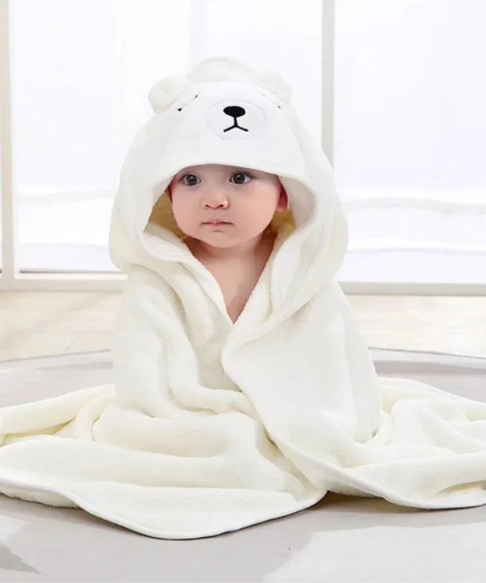 Bébé portant un poncho de bain blanc à capuche ours en peluche, assis sur un tapis.