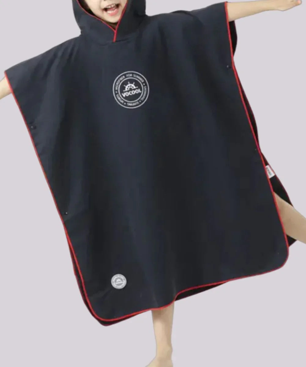 Garçon portant un poncho de bain noir à capuche avec bordure rouge, idéal pour la plage.