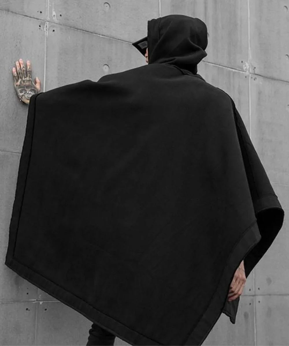 Poncho homme noir avec capuche, style moderne, contre un mur en béton.