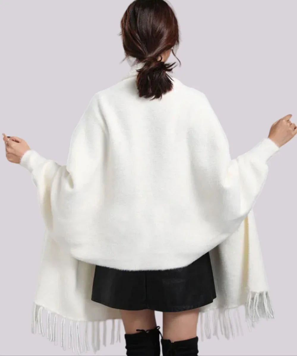 Femme de dos portant un poncho blanc élégant avec franges, jupe noire et bottes