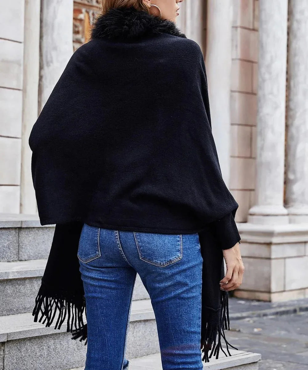 Femme portant un poncho noir à col fourrure et franges, jeans, extérieur urbain.