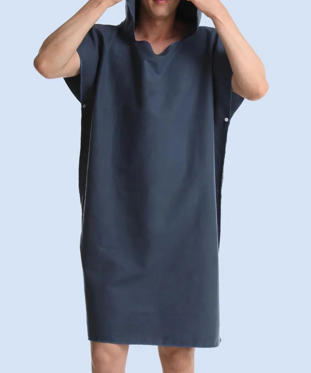 Homme portant un poncho serviette surf bleu à capuche, fond uni bleu clair.