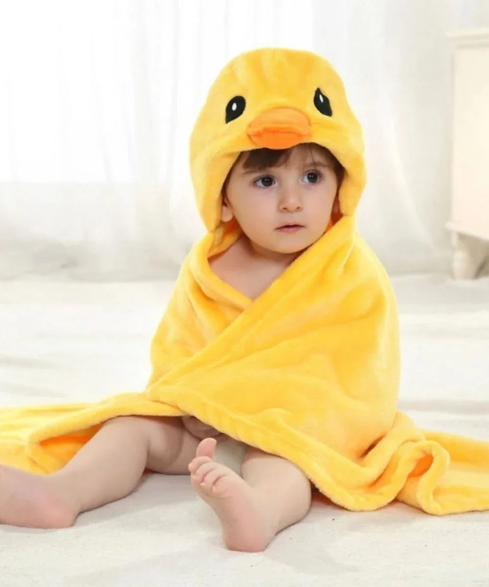 Bébé portant un poncho de bain jaune en forme de canard, assis sur un tapis blanc.