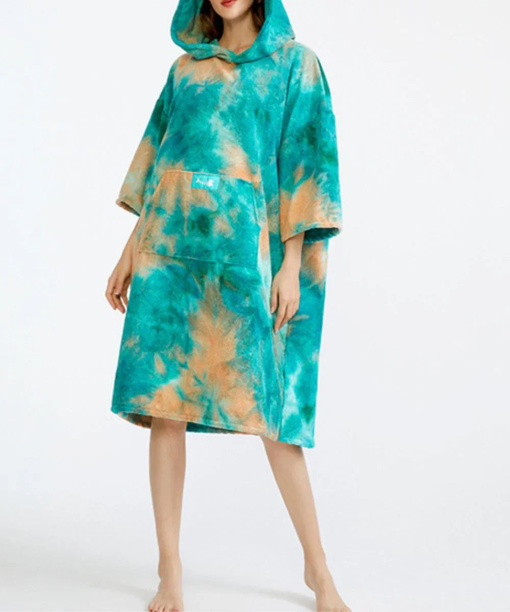 Femme portant un poncho de bain vert et orange à capuche, motif tie-dye, sur fond blanc.