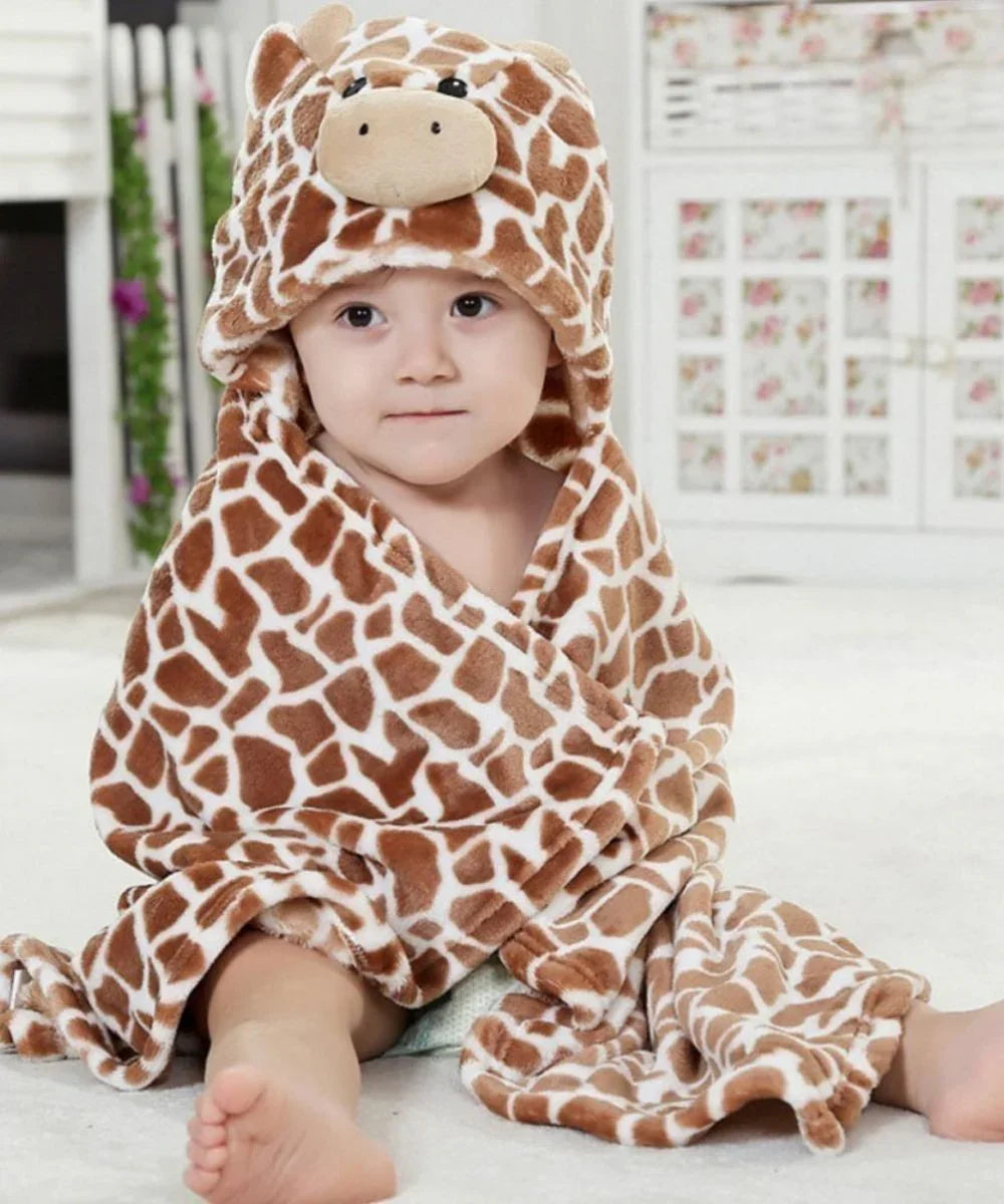 Bébé portant un poncho de bain à capuche motif girafe, assis sur un tapis blanc.