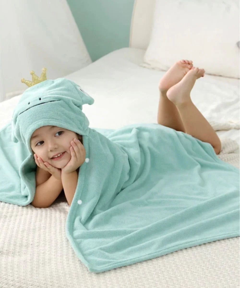 Enfant allongé sur un lit portant un poncho de bain turquoise à capuche grenouille couronnée