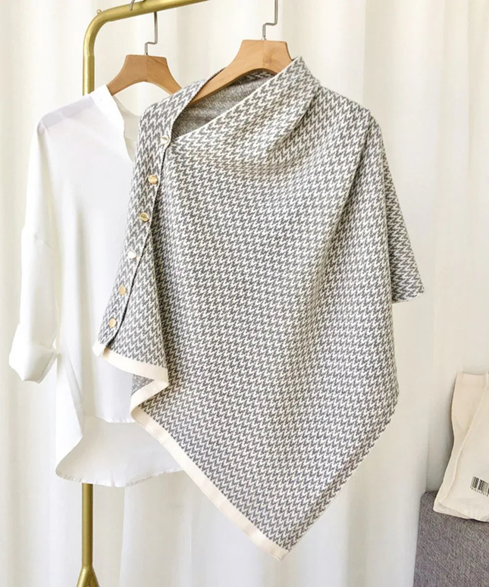 Poncho femme boutonné à motif pied-de-poule gris et blanc, suspendu sur cintre.