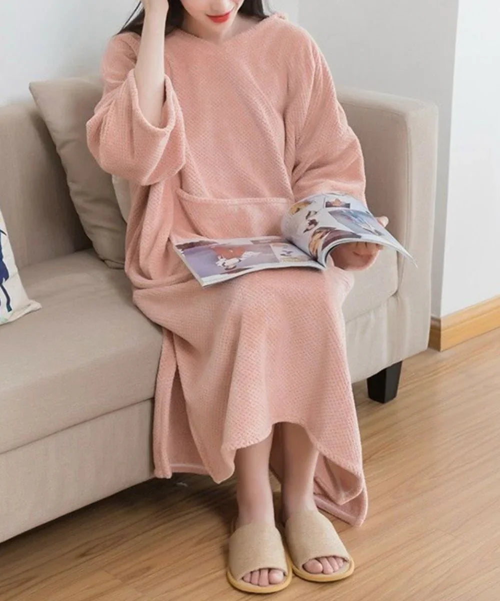 Femme assise portant un poncho de bain rose à capuche, assise sur un canapé et lisant un magazine