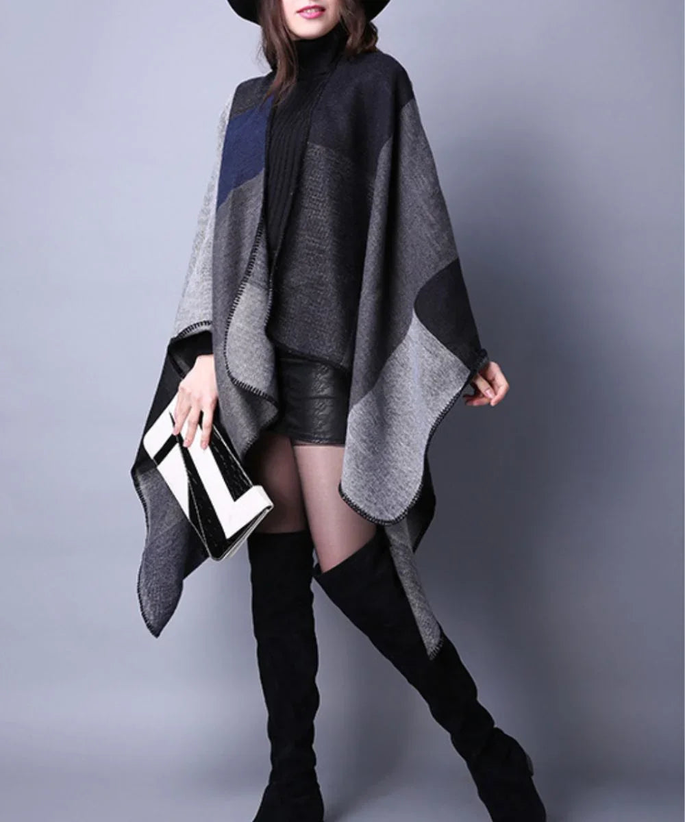 Femme portant un poncho gris élégant, short noir, cuissardes et chapeau, fond neutre.