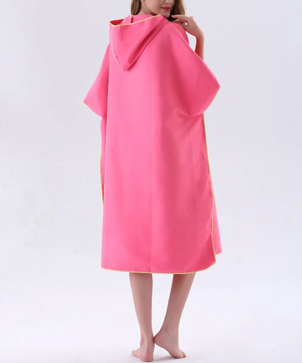 Poncho kitesurf femme rose à capuche, porté par une femme pieds nus, fond blanc minimaliste