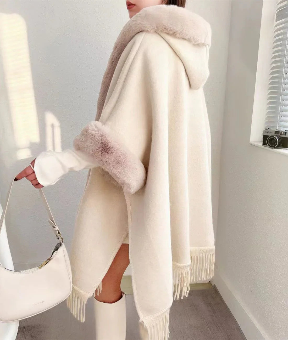 Femme portant un poncho polaire beige à capuche et bordure en fausse fourrure, look hivernal élégant
