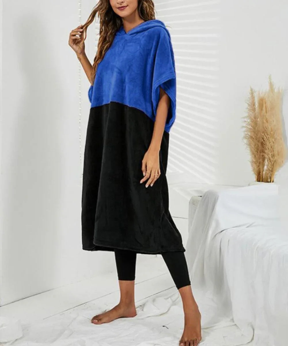 Femme portant un poncho serviette bicolore bleu et noir à capuche, dans une chambre lumineuse.
