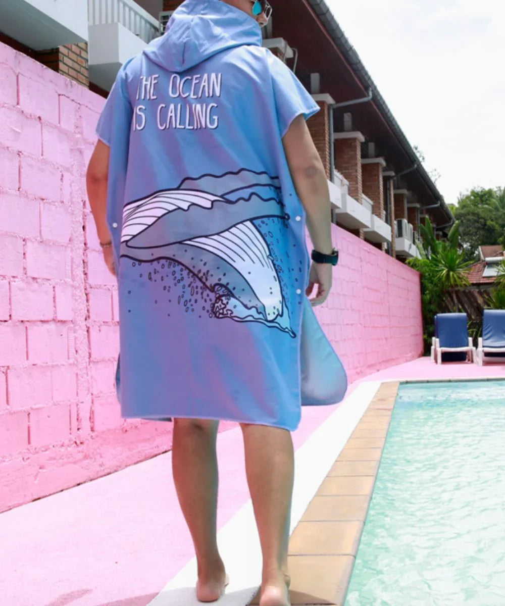 Poncho de surf bleu avec capuche, motif vague et texte, porté près d'une piscine