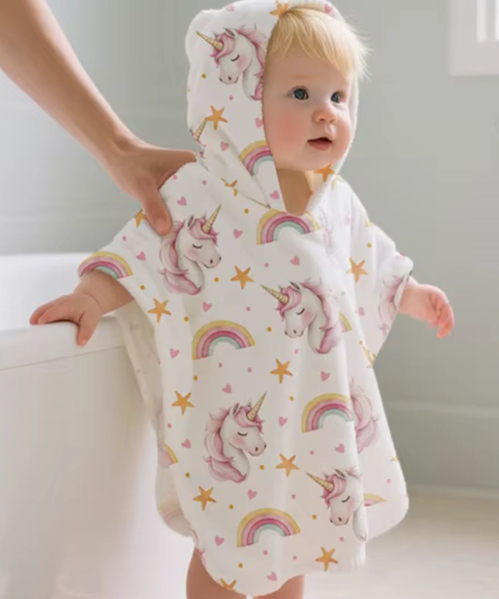Bébé fille portant un poncho serviette à capuche Planète Poncho avec motifs licornes et arcs-en-ciel
