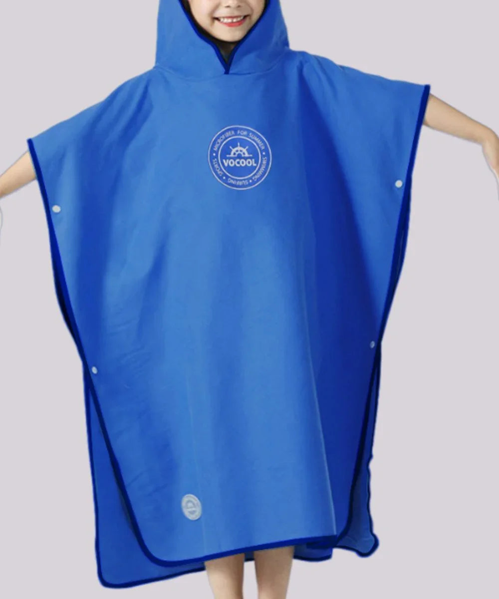 Enfant souriant portant un poncho surf bleu à capuche, adapté à la plage ou à la piscine.