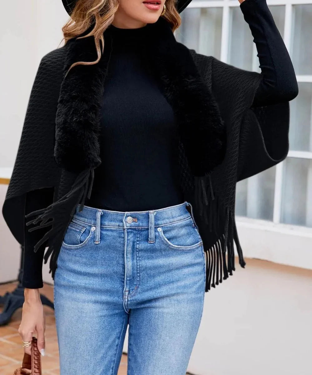 Poncho noir femme à franges et col en fausse fourrure, porté avec jean bleu.